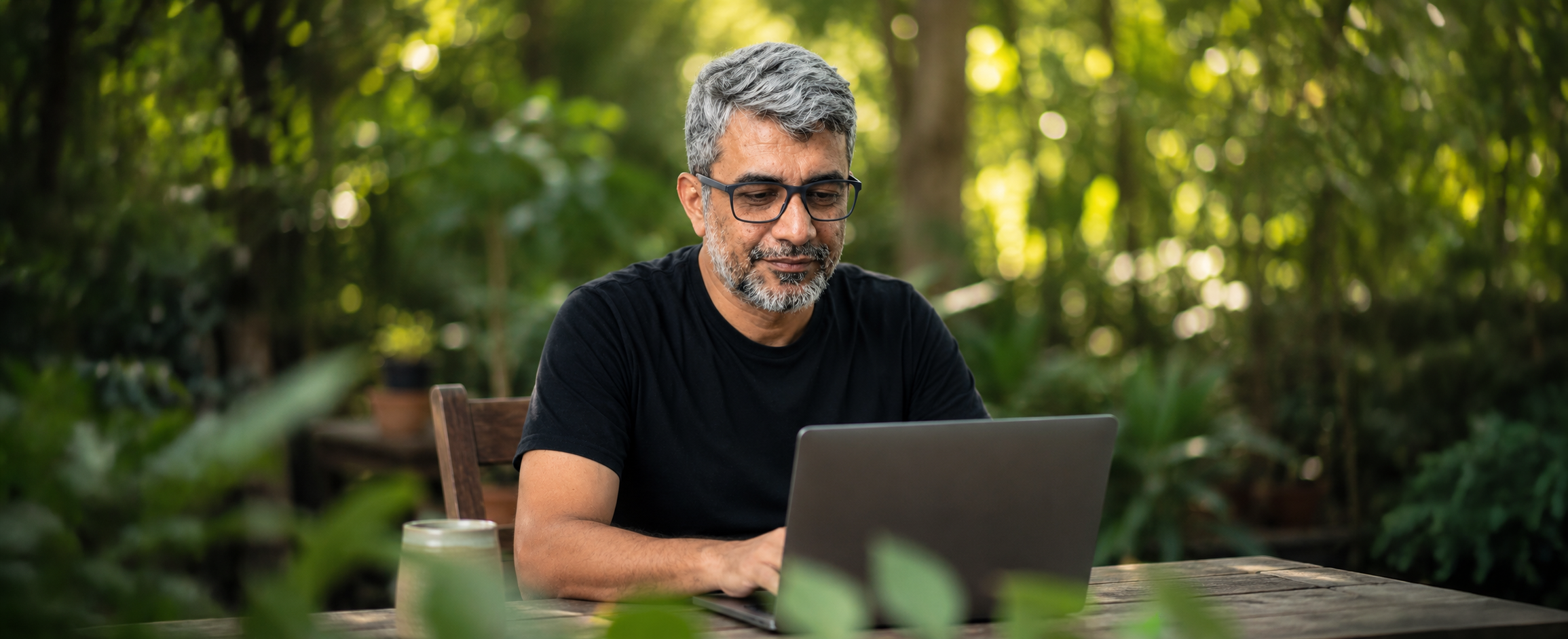 Santhosh Kumar working on a laptop in a green outdoor setting